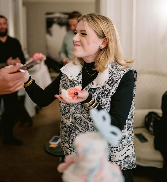 Woman smiling while holding cake piece at a gathering; related to viral wedding and pregnancy news.