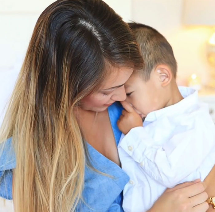 Woman holding a young boy, both looking down, in a tender moment.