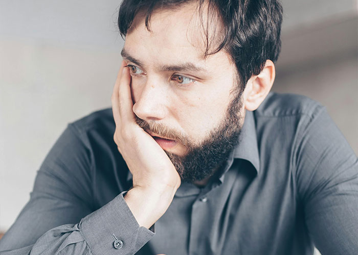 Man in a grey shirt looking thoughtful, possibly recalling an awkward job interview experience.