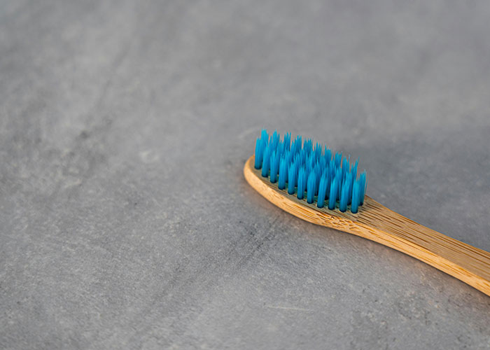 Bamboo toothbrush with blue bristles on a gray surface, related to awkward job interviews.