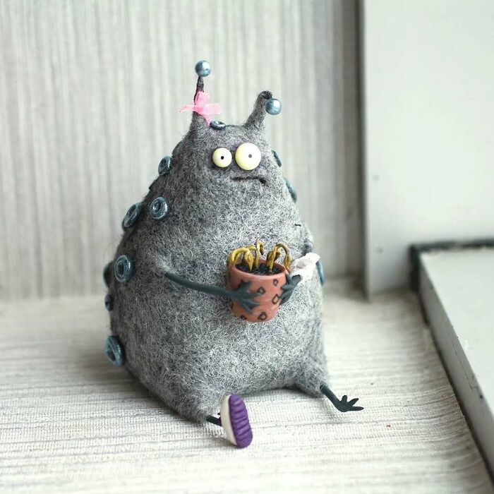 Funny-looking animal art doll by Georgian artist, featuring a grey fuzzy creature with button decorations and holding a mug.