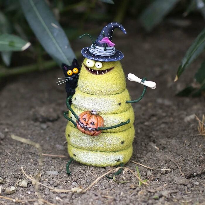 Funny-looking strange art doll resembling a caterpillar with a witch hat, holding a pumpkin, created by a Georgian artist.