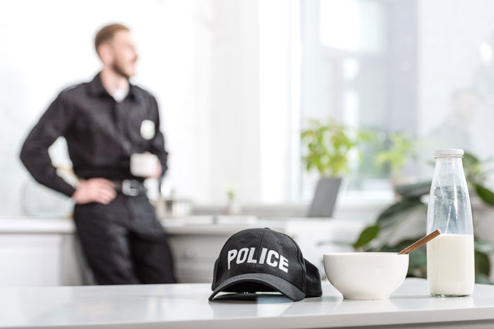 Police cap on a table with milk and cereal, officer in background, related to apartment scam incident.