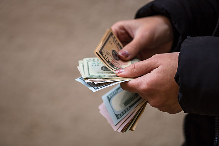 Hands holding a stack of US dollar bills, related to an apartment scam and unexpected revenge.