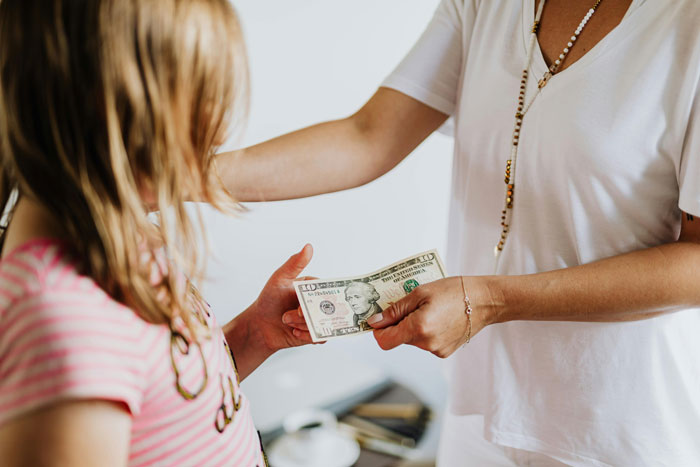 Child receiving money from adult for chores, highlighting debate on paying children for household tasks.