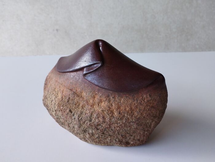 A smooth sculpture resembling soft fabric placed on a textured stone, demonstrating physics-defying artistry.