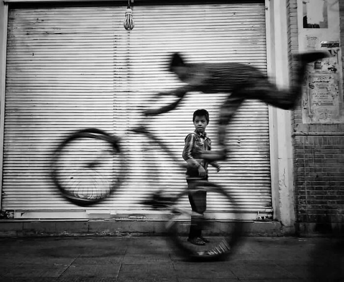 A child stands near a blurred cyclist in front of a metal shutter, capturing an interesting moment.