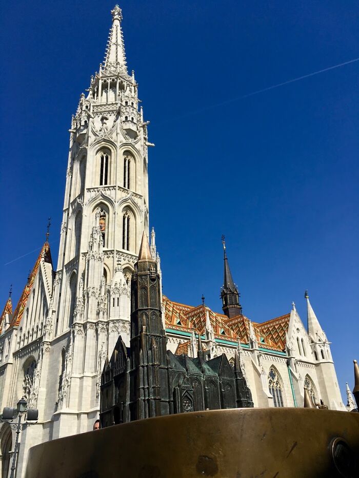 Gothic church under clear blue sky with ornate tower and miniature replica in the foreground, showcasing fascinating architecture.