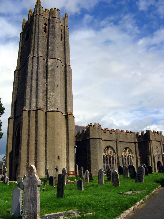 Tall historic church tower surrounded by gravestones under a cloudy sky.