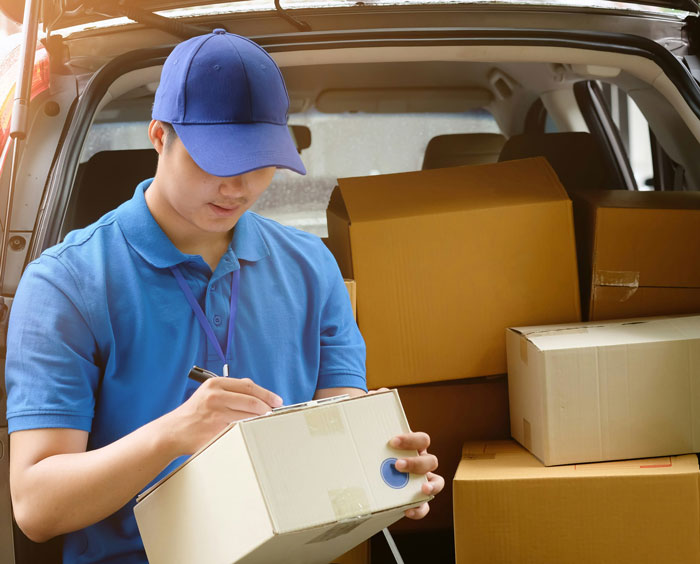 Amazon driver wearing a blue uniform writing a note beside delivery boxes in a vehicle.