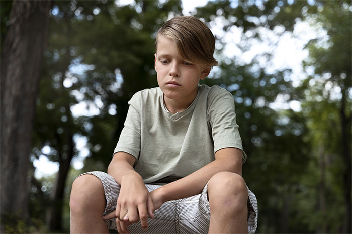 Teen sitting outdoors, looking thoughtful, representing refusal to be treated as family's babysitter.