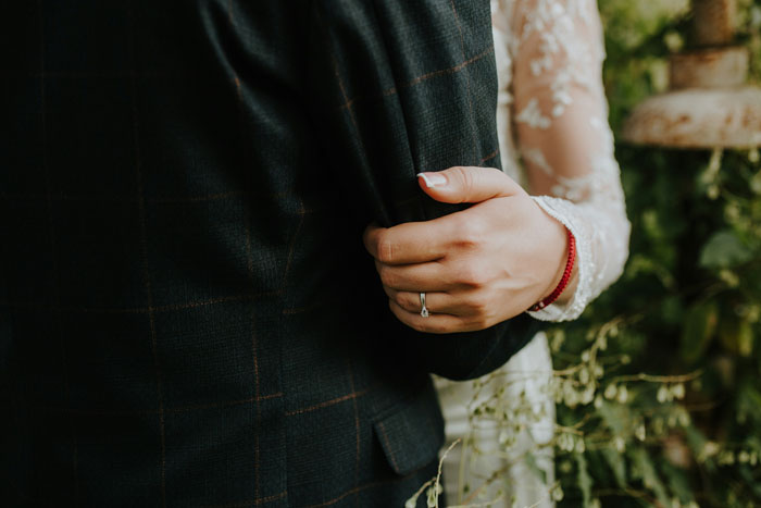 A woman in a lace dress gently holds a man's arm in a suit, symbolizing a complex relationship scenario.