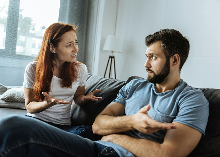 Man and woman in a heated discussion on a couch, both gesturing with their hands.