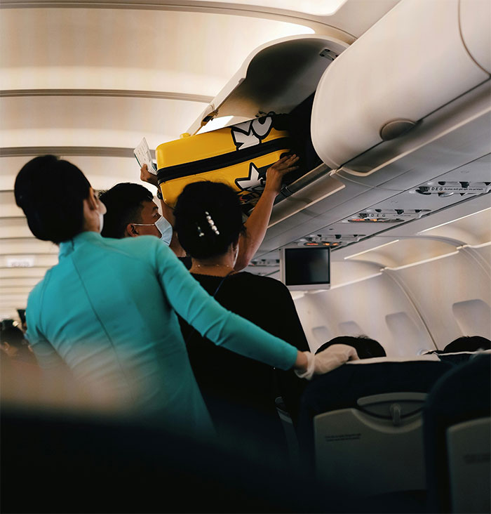 Passengers on an airplane deplaning, with a man placing luggage in an overhead bin, following a row-by-row exit rule.