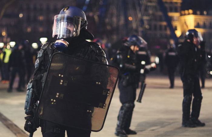 Police officers in riot gear standing in formation during a nighttime protest.