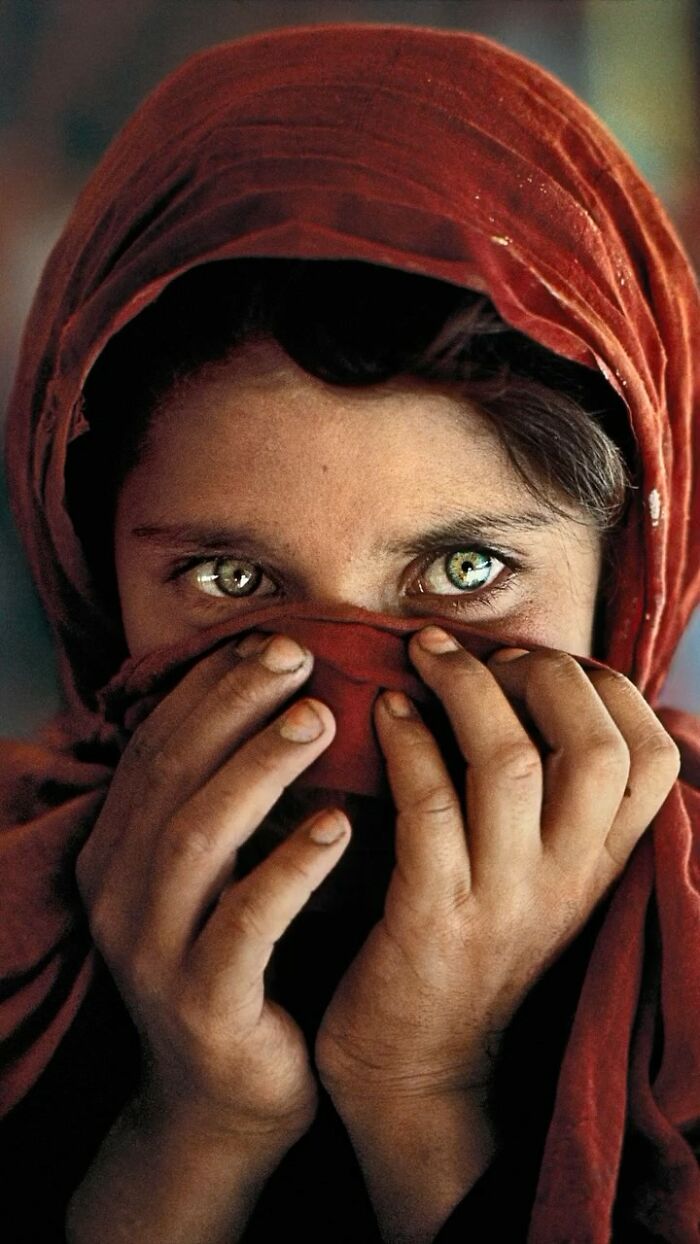 A compelling image of a person with striking green eyes, partially covering their face with a red cloth.