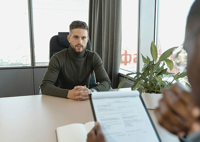 Candidate in a job interview, sitting at a desk, appearing slightly nervous.