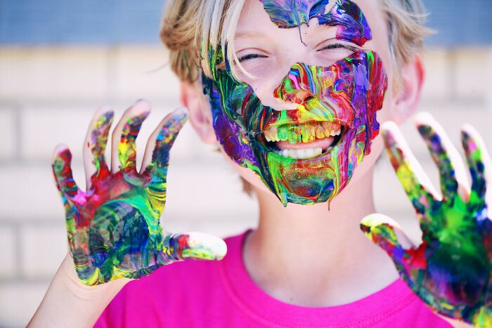 Child smiling with colorful paint on face and hands, showcasing creativity and joy.