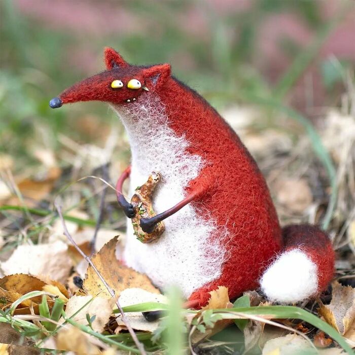 Strange art doll of a quirky animal with red fur, created by a Georgian artist, sitting among autumn leaves.