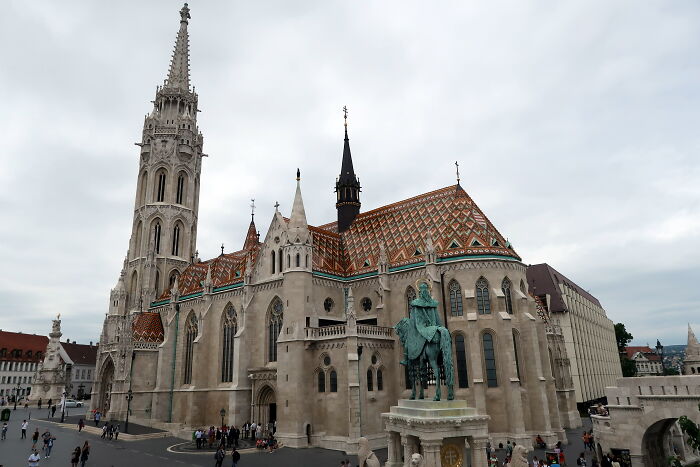 Gothic church with ornate roof and tall spire, people in the square, showcasing fascinating architecture.