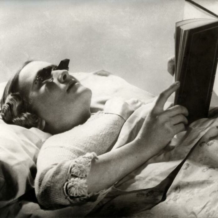 Person using a historical invention, a bed prism for reading while lying down, showcasing innovation ahead of its time.