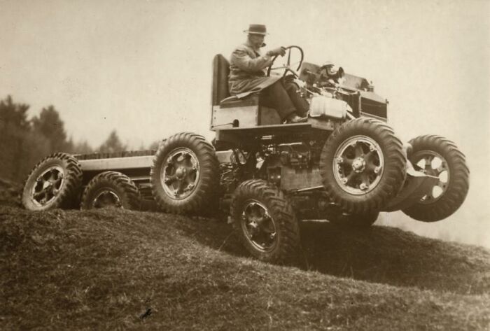 Person driving an early multi-wheeled vehicle on rough terrain, showcasing historical inventions.