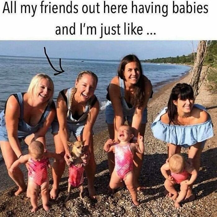 Dog owner holding a dog in swimsuit among friends with babies on the beach, illustrating relatable humor for dog lovers.