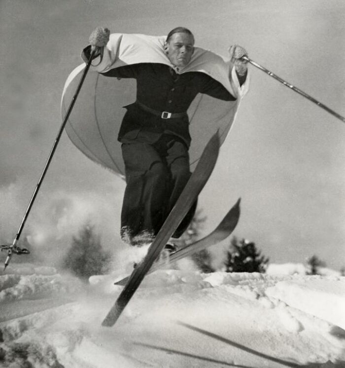 A man skiing with an early parachute-style invention, highlighting historical innovations on the snow.