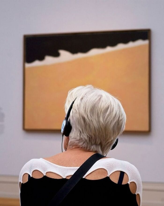 Woman with headphones viewing an interesting painting at a gallery.