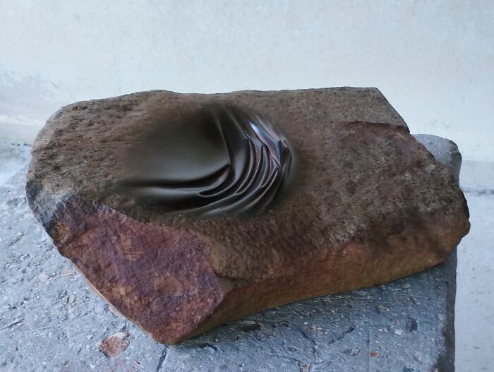 Stone sculpture with fluid folds, appearing soft and defying physics, showcased on a concrete surface.