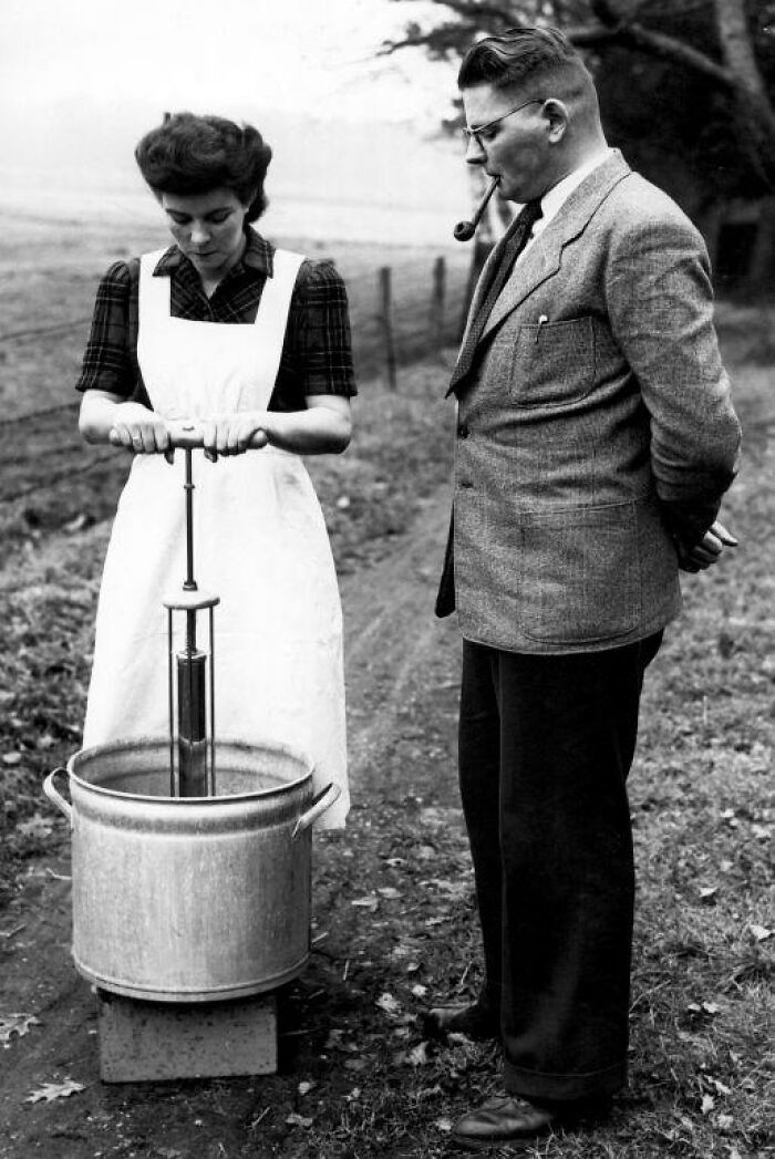 Woman using a historical butter churn, observed by man, representing inventions ahead of their time.