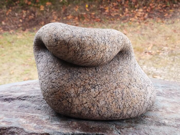 Smooth stone sculpture bending gracefully on a rock, showcasing the illusion of softness.