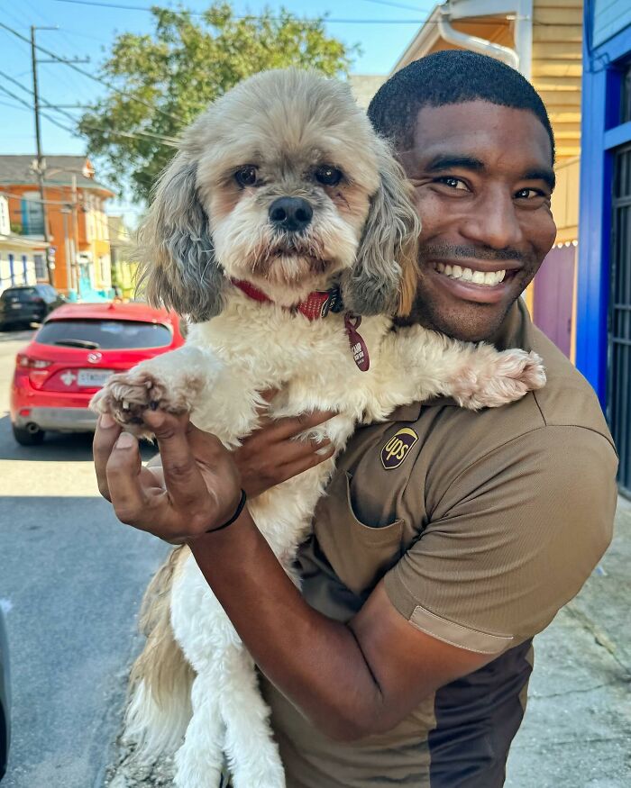 UPS driver smiling while holding an adorable fluffy dog on his route.