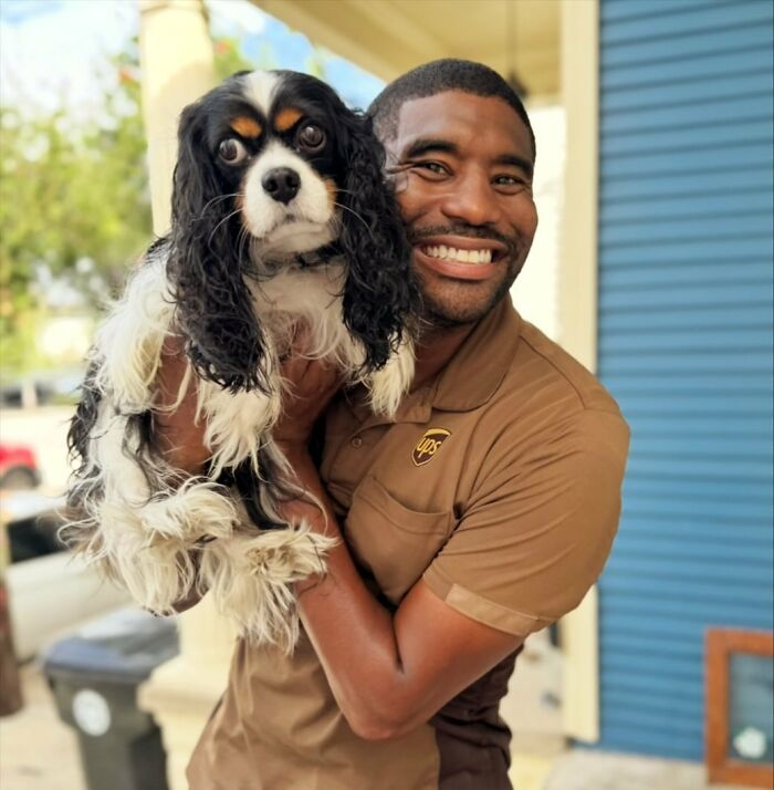 UPS driver smiling while holding a cute dog during his delivery route.