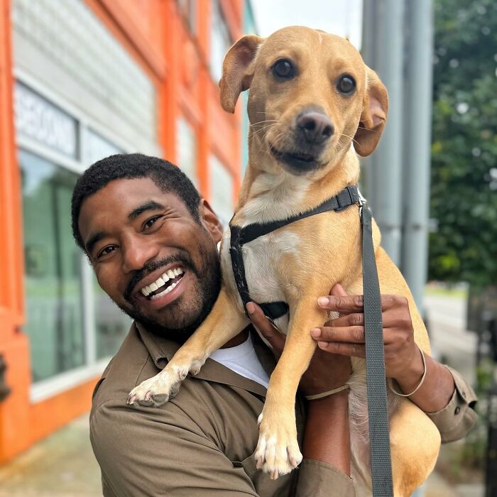 UPS driver smiling and holding an adorable dog on his route.