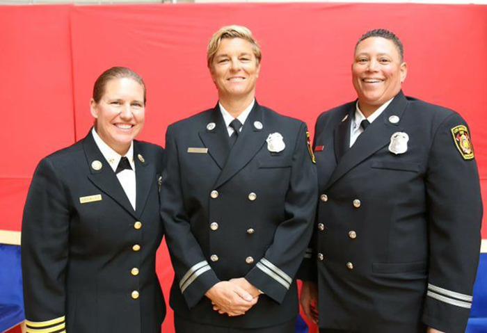 Three female firefighter leaders in uniform smiling against a red background.