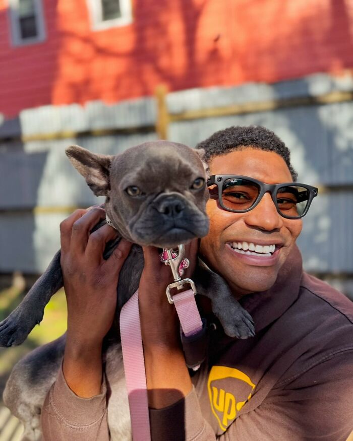 UPS driver smiling, holding a cute dog on his delivery route.