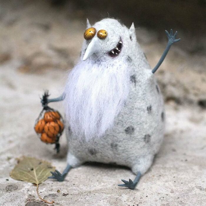 Funny-looking animal doll with long white beard and big eyes, holding a tiny pumpkin, made by a Georgian artist.