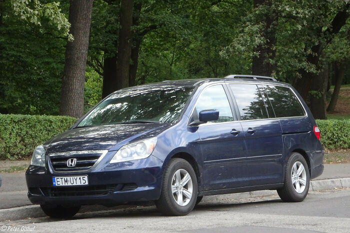 Blue Honda minivan parked on a tree-lined street, showcasing intriguing facts about everyday cars.