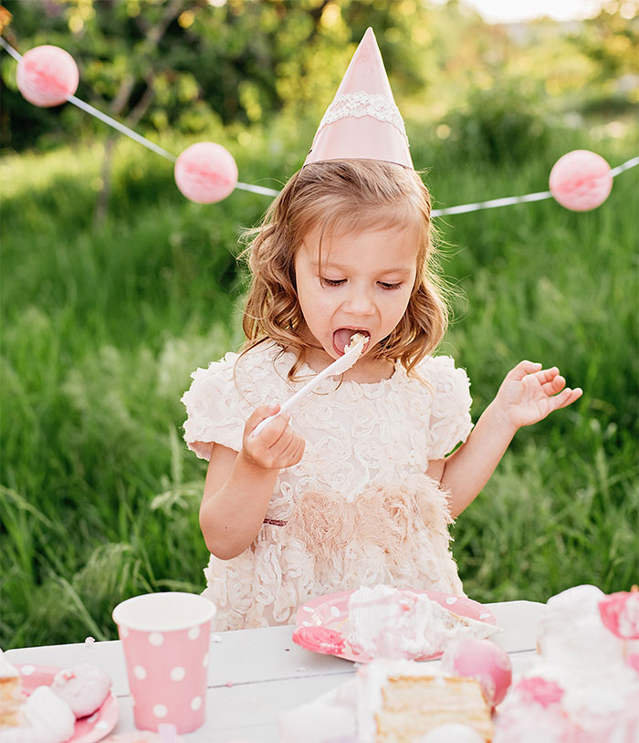 A child at a pink-themed party eating dessert, wearing a pink party hat.