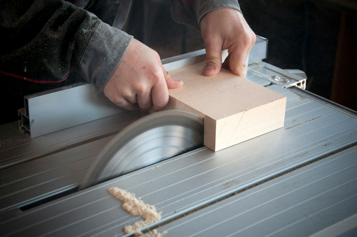 Person cutting wood on a table saw, showcasing craftsmanship and precision.