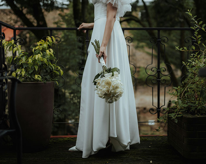 Bride in wedding dress holding bouquet, standing by a railing, representing a wedding scam.