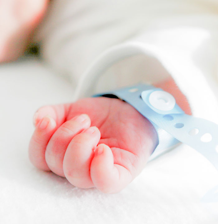 Newborn's hand with hospital ID band in NICU, highlighting care and monitoring.