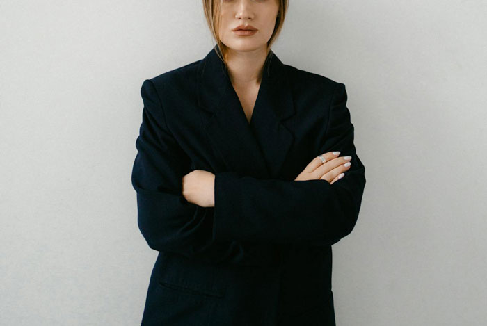 A person in a dark blazer with arms crossed, presenting a confident stance.