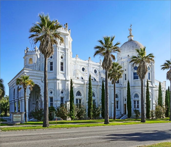 A stunning white church surrounded by tall palm trees under a clear blue sky, showcasing fascinating architecture.