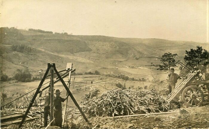 Two men working with historical machinery in a rural landscape, showcasing early inventive technology.