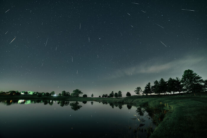 Meteor shower reflecting over a calm lake, showcasing stunning natural phenomena against a starry night sky.