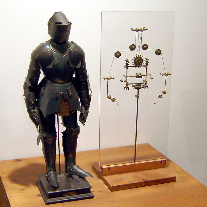 Armor-clad historical invention displayed alongside mechanical components on a wooden table.