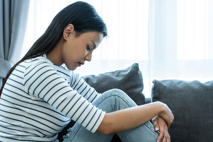 A woman in a striped shirt, sitting on a couch, appearing thoughtful; traumatize is the SEO keyword here.