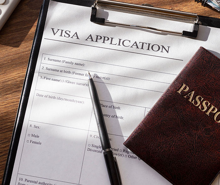 “Visa application form and passport on a wooden desk, symbolizing international travel or documentation process.”